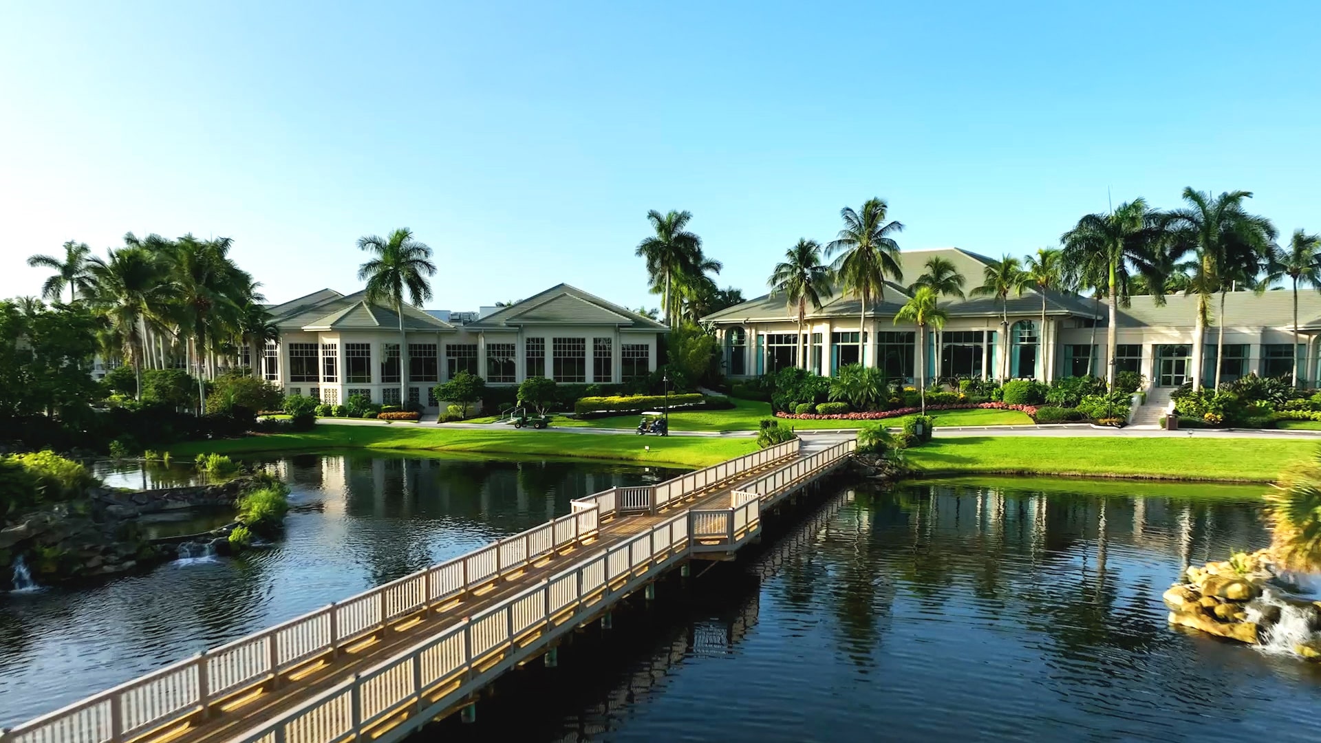The Boca West clubhouses across a lake with a wooden footbridge
