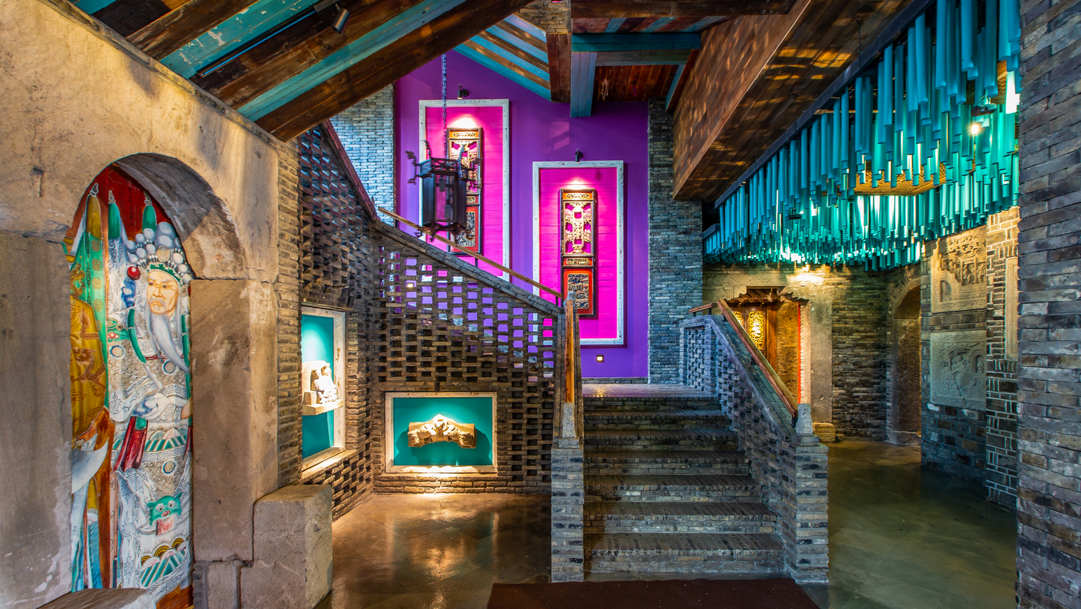 The museum's brick stair hall, lit in magenta and teal, with carved artefacts in illuminated niches