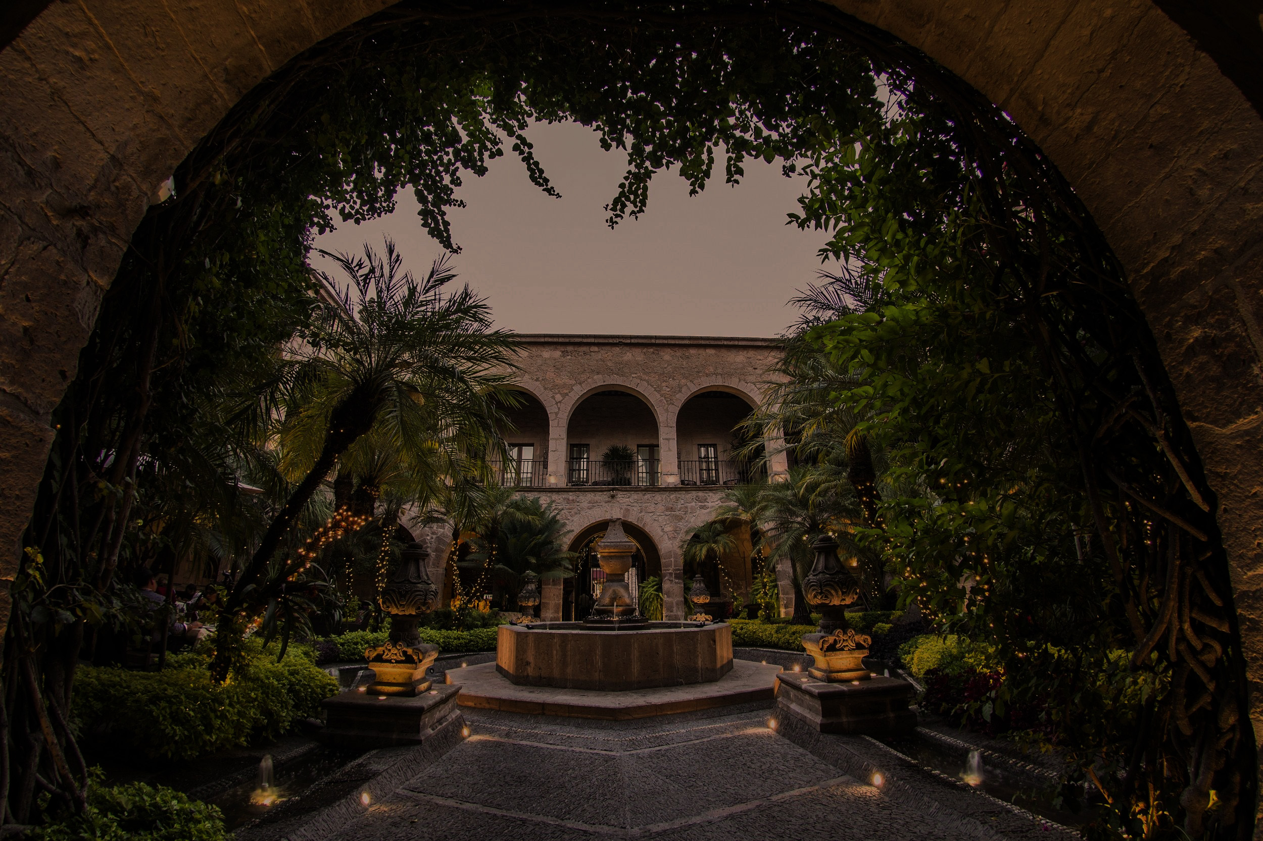 A dusk-lit boutique hotel courtyard framed by a stone arch